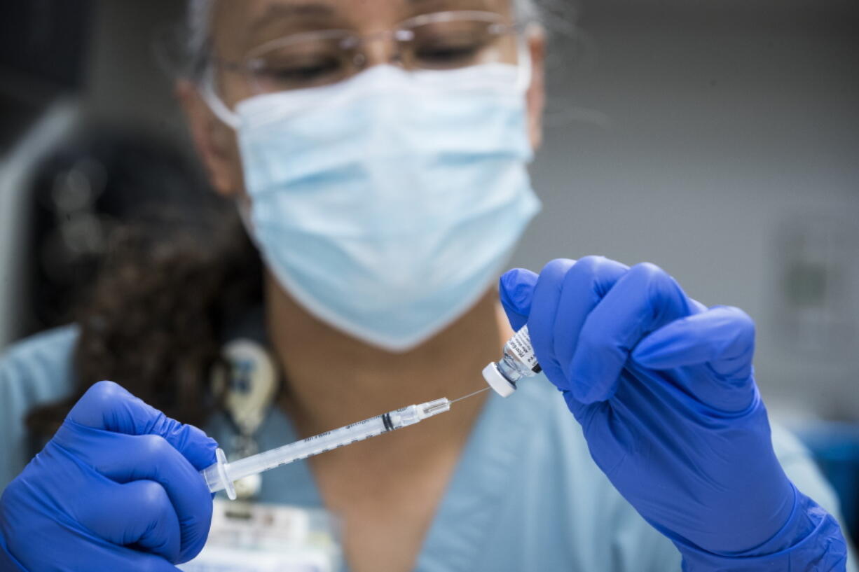 FILE - In this Thursday, Feb. 11, 2021 file photo, pharmacy technician Sochi Evans fills a syringe with a Pfizer-BioNTech COVID-19 vaccine at Texas Southern University in Houston. Coronavirus cases are continuing to decline in the U.S. after a winter surge. Researchers at Johns Hopkins University say the seven-day average of new coronavirus cases in the country dropped below 100,000 on Friday, Feb. 12 for the first time since November 4.