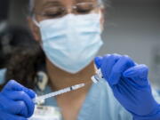 FILE - In this Thursday, Feb. 11, 2021 file photo, pharmacy technician Sochi Evans fills a syringe with a Pfizer-BioNTech COVID-19 vaccine at Texas Southern University in Houston. Coronavirus cases are continuing to decline in the U.S. after a winter surge. Researchers at Johns Hopkins University say the seven-day average of new coronavirus cases in the country dropped below 100,000 on Friday, Feb. 12 for the first time since November 4.