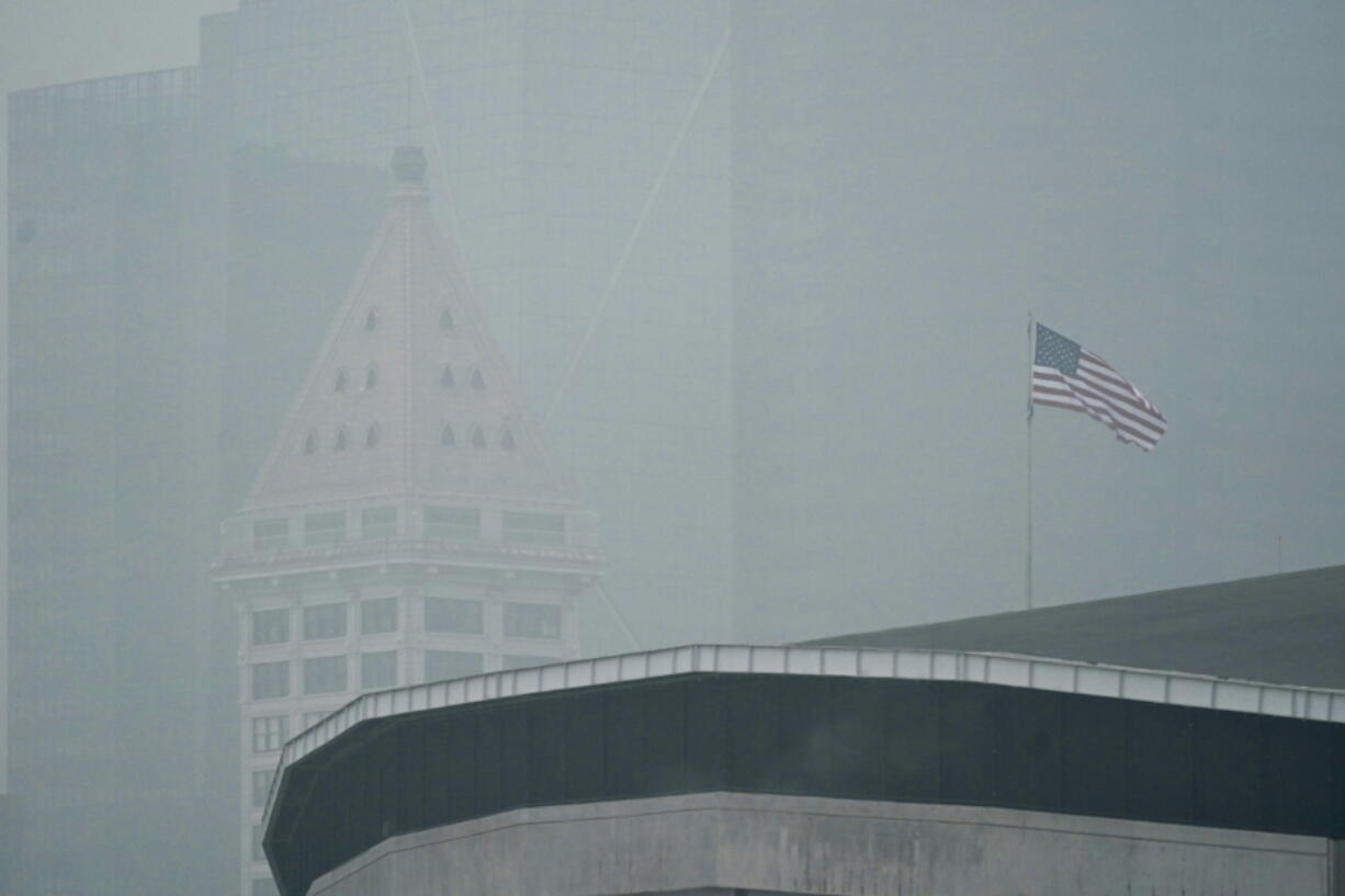 FILE - In this Sept. 14, 2020, file photo, a U.S. flag flies near Smith Tower in downtown Seattle as air thick with smoke from wildfires as seen over CenturyLink Field in Seattle. The damage caused by wildfires can be devastating, yet researchers say the smoke from the annually recurring blazes also delivers economic damage to areas that were never touched by the flames. (AP Photo/Ted S.