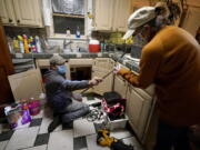 FILE - In this Feb. 20, 2021, file photo, Handyman Roberto Valerio, left, hands homeowner Nora Espinoza the broken pipe after removing it from beneath her kitchen sink in Dallas. The pipe broke during freezing temperatures brought by last week&#039;s winter weather.