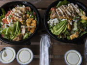 Avo-Cobb-O salads from Red Robin Gourmet Burgers and Brews, left, and Fresh Set are pictured in their delivery packaging. Fresh Set is one of three &quot;virtual brands&quot; from Red Robin that operates exclusively on delivery apps like DoorDash. At top, the salads are shown listed at Red Robin, left, and Fresh Set on the DoorDash app.