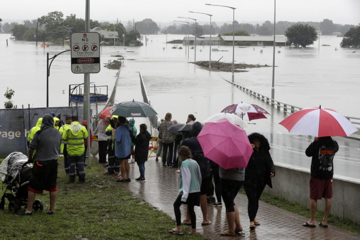 People shelter under umbrellas as they watch the flooded Hawkesbury River in Windsor, northwest of Sydney, New South Wales, Australia, Monday, March 22, 2021. Hundreds of people have been rescued from floodwaters that have isolated dozens of towns in Australia&#039;s most populous state New South Wales and forced thousands to evacuate their homes as record rain continues.