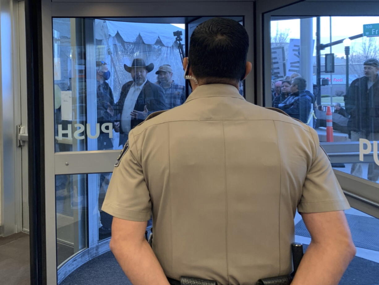 Anti-government activist Ammon Bundy, wearing a cowboy hat, yells through the closed Ada County Courthouse door at law enforcement officers inside Monday, March 15, 2021, in Boise, Idaho. Bundy was scheduled to stand trial Monday on charges that he trespassed and obstructed officers at the Idaho Statehouse during a special legislative session last fall, but Magistrate Judge David Manweiler issued a warrant for Bundy&#039;s arrest after Bundy failed to appear in the courtroom. People are required to wear face coverings while at the courthouse because of the coronavirus pandemic, but Bundy and several others were protesting the mask requirement.