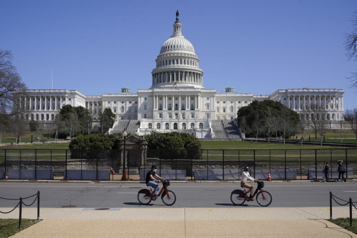 Bicyclists ride past an inner perimeter of security fencing on Capitol Hill in Washington, Sunday, March 21, 2021, after portions of an outer perimeter of fencing were removed overnight to allow public access.