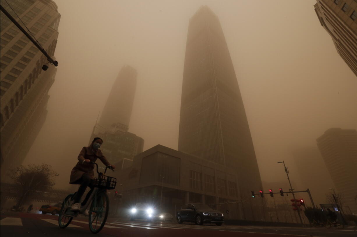 A cyclist and motorists move past office buildings amid a sandstorm during the morning rush hour in the central business district in Beijing, Monday, March 15, 2021. The sandstorm brought a tinted haze to Beijing&#039;s skies and sent air quality indices soaring on Monday.