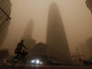 A cyclist and motorists move past office buildings amid a sandstorm during the morning rush hour in the central business district in Beijing, Monday, March 15, 2021. The sandstorm brought a tinted haze to Beijing&#039;s skies and sent air quality indices soaring on Monday.