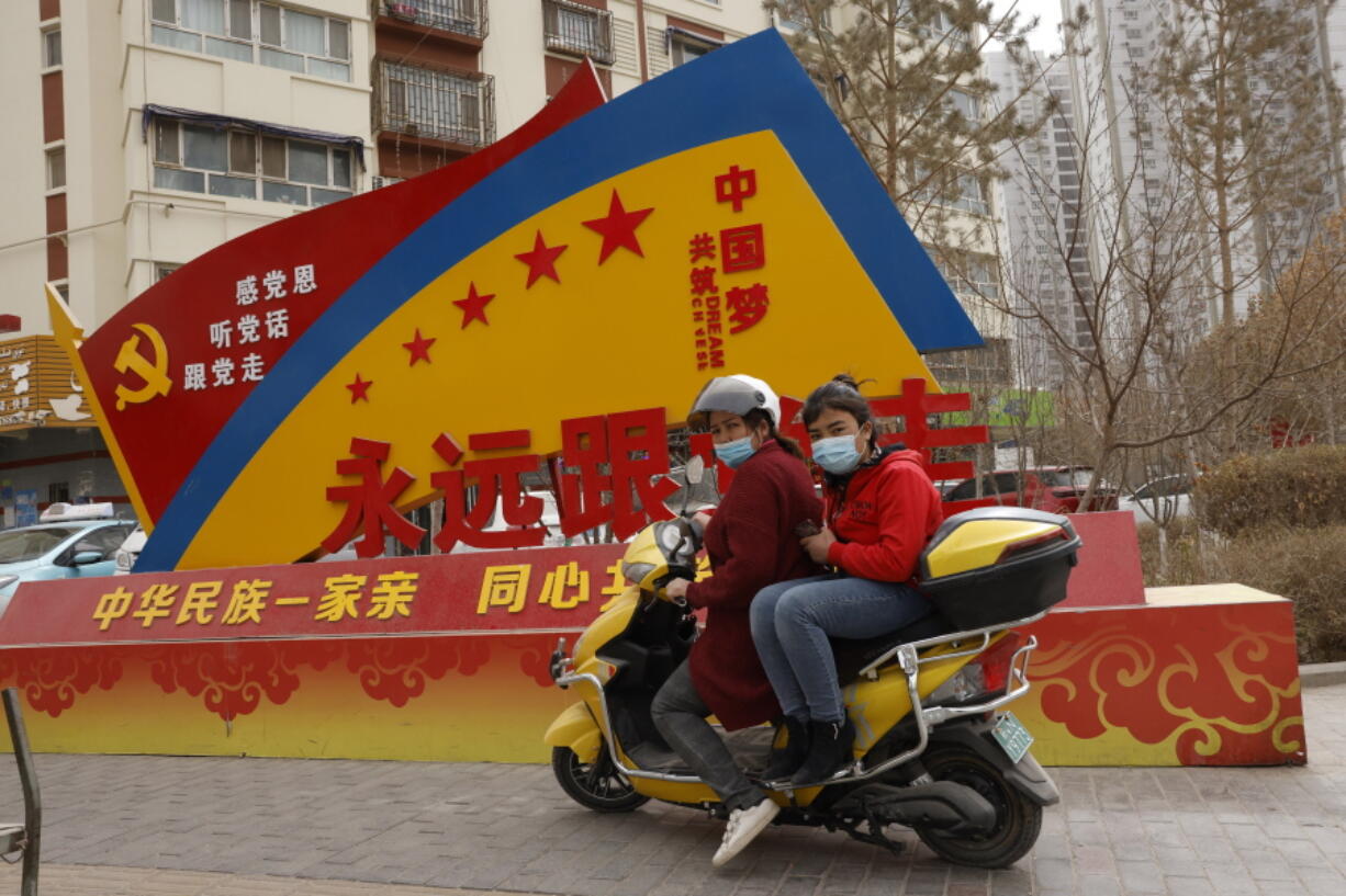 Residents wearing masks pass by  government propaganda with slogans some of which read &quot;Forever follow the Party&quot; and &quot;China&#039;s Ethnicities One Family&quot; in the city of Aksu in western China&#039;s Xinjiang region on Thursday, March 18, 2021. China on Friday announced sanctions on British individuals and entities following the U.K.&#039;s joining the EU and others in sanctioning Chinese officials accused of human rights abuses in the Xinjiang region.