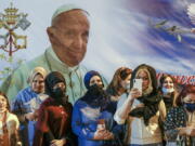 Women wait outside the Chaldean Cathedral of Saint Joseph, in Baghdad, Iraq, Saturday, March 6, 2021, where Pope Francis, depicted on a giant poster at their back, is concelebrating a mass. Earlier today Francis met privately with the country&#039;s revered Shiite leader, Grand Ayatollah Ali al-Sistani.