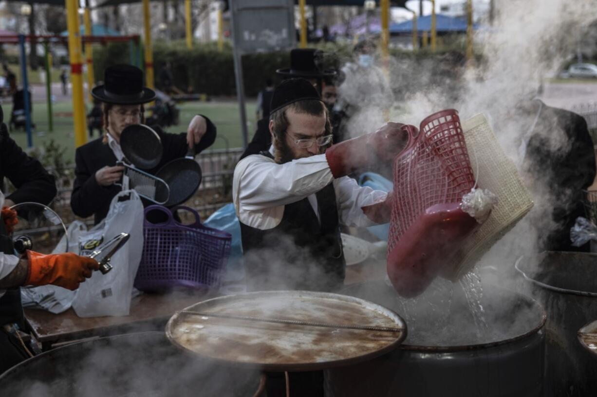 An ultra-Orthodox Jewish man dips cooking utensils in boiling water to remove remains of leaven in preparation for the upcoming Jewish holiday of Passover in Ashdod, Israel, Thursday, March 25, 2021.  Israelis will once again hold large family gatherings this weekend to celebrate Passover, the festive Jewish holiday recalling the biblical flight of the Israelites from Egypt.