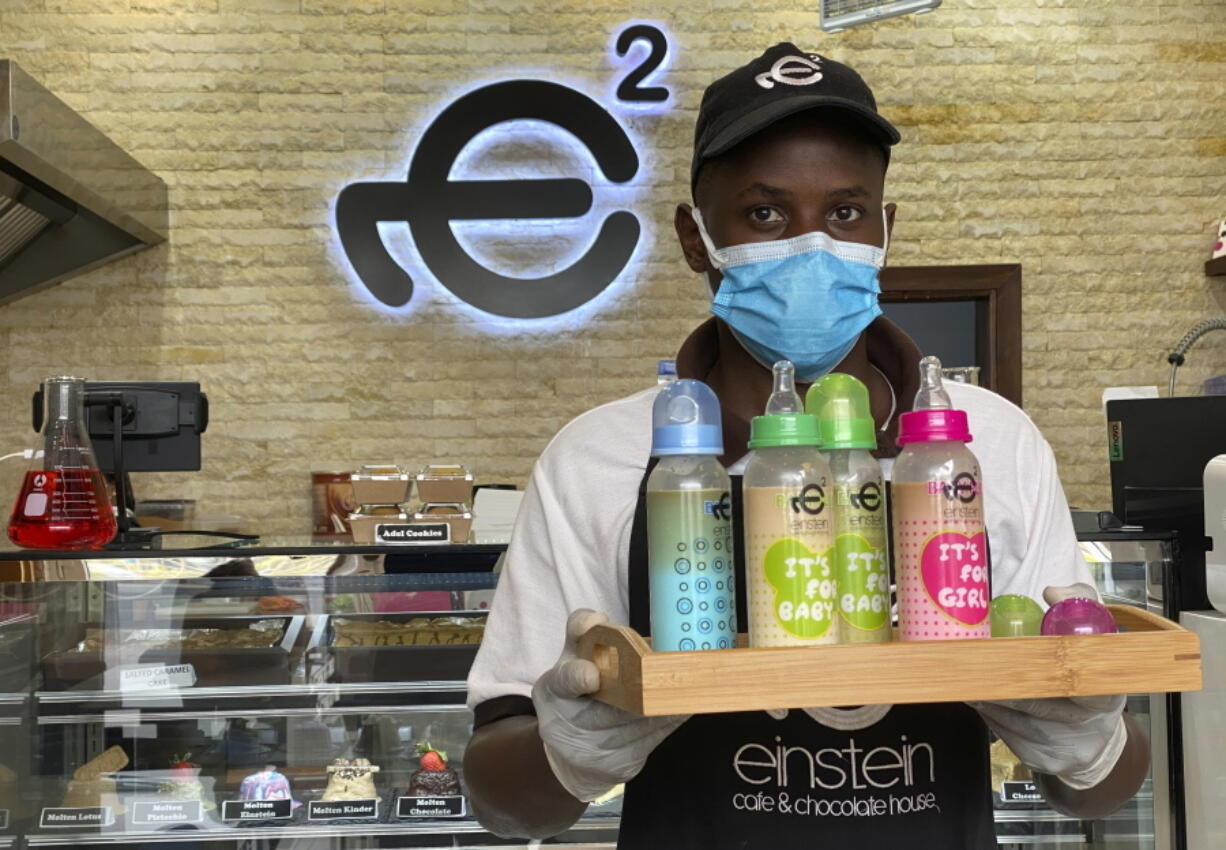 A waiter poses with a tray of baby bottles that he brought out from storage, at Einstein Cafe in Dubai, United Arab Emirates, Sunday, March 14, 2021. Cafes across several Gulf Arab states have begun selling coffee and other cold drinks in baby bottles, kicking off a new trend that has prompted excitement, confusion and backlash. The fad started at Einstein Cafe, a slick dessert chain with branches across the region. Soon, authorities from Kuwait to Dubai cracked down claiming the trend violates local traditions.