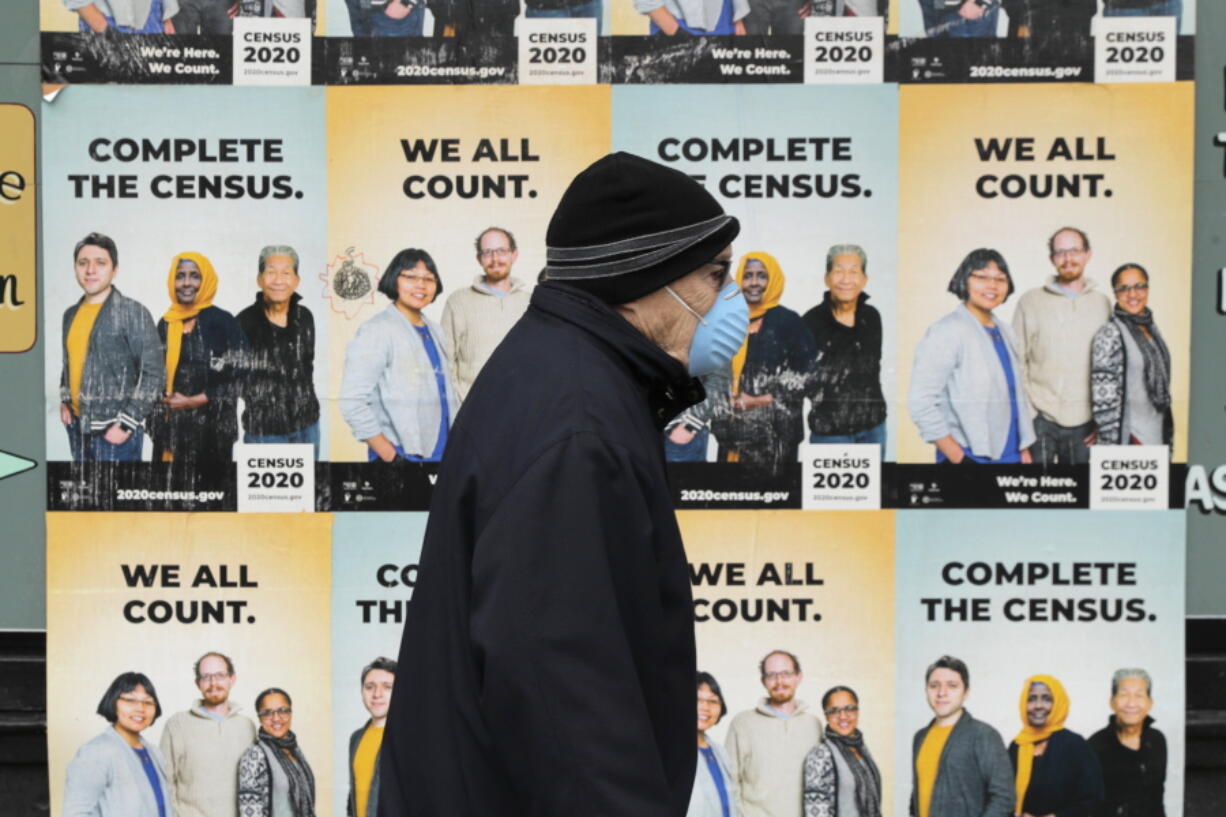 FILE - In this April 1, 2020, file photo, a man wearing a mask walks past posters encouraging participation in the 2020 Census in Seattle&#039;s Capitol Hill neighborhood. A delay in census data is scrambling plans in some states to redraw districts for the U.S. House and state legislatures. The Census Bureau has said redistricting data that was supposed to be provided to states by the end of March won&#039;t be ready until August or September. (AP Photo/Ted S.