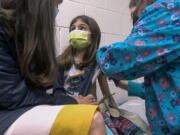 In this Wednesday, March 24, 2021 image from video provided by Duke Health, Alejandra Gerardo, 9, looks up to her mom, Dr. Susanna Naggie, as she gets the first of two Pfizer COVID-19 vaccinations during a clinical trial for children at Duke Health in Durham, N.C. In the U.S. and abroad, researchers are beginning to test younger and younger kids, to make sure the shots are safe and work for each age.