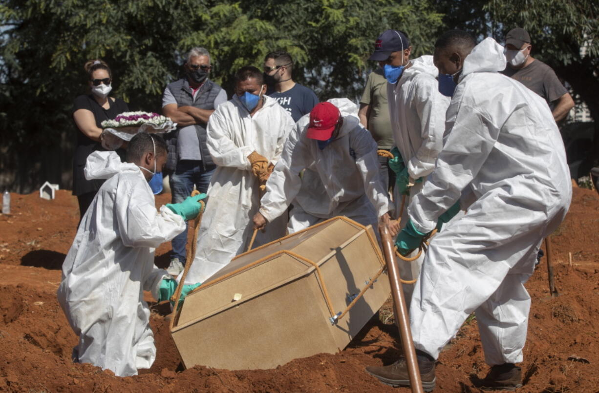 Cemetery workers in full protective gear lower a coffin that contain the remains of a person who died from complications related to COVID-19 at the Vila Formosa cemetery in Sao Paulo, Brazil, Wednesday, March 24, 2021.