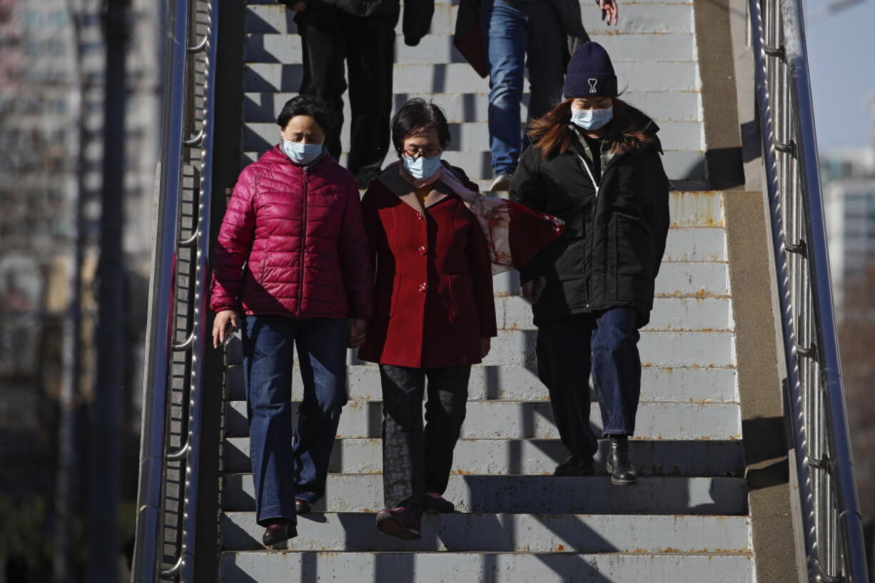 People wearing face masks to help curb the spread of the coronavirus walk down a pedestrian overhead bridge in Beijing, Sunday, March 21, 2021.