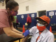 Debbie Monahan, a school nurse, pulls down Charles Robbins&#039; sleeve after giving him his second shot of the coronavirus vaccine at Surry County High School in Dendron, Va., on Saturday Feb. 27, 2021. Getting the coronavirus vaccine has been a challenge for rural counties in the U.S. that lack medical facilities such as a pharmacy or a well-equipped doctor&#039;s office.