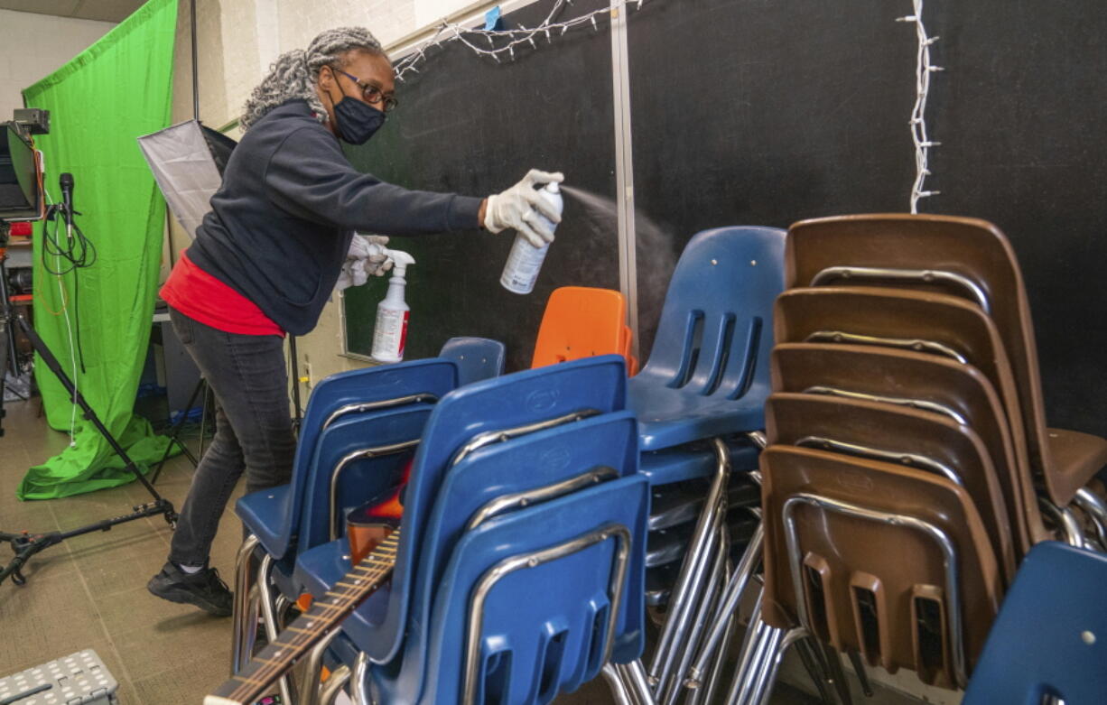 FILE - In this Thursday, March 4, 2021, file photo, Latisha Bledsoe cleans chairs in the music room at Manchester Academic Charter School during the coronavirus pandemic in Pittsburgh. The school is planning to return students to the classroom in a hybrid schedule at the end of March.