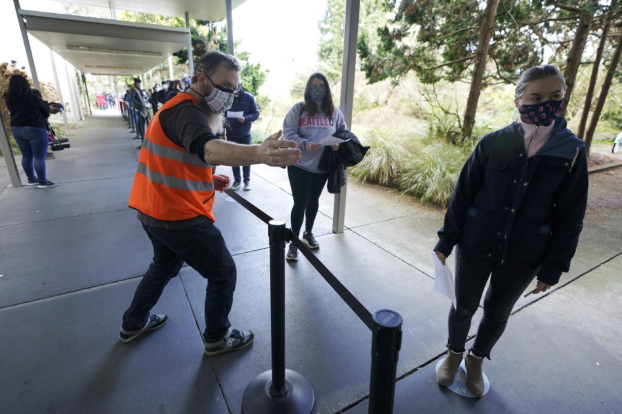 Volunteer worker Pete Graham, left, helps direct newly arriving volunteers to a health screening station, Friday, Feb. 26, 2021, at a mass vaccination clinic at Seattle University in Seattle near the end of his shift. After finishing his shift, Graham was able to get the first dose of the Moderna COVID-19 vaccine in return for his labor. As states ramp up vaccination distribution in the fight against the coronavirus, volunteers are needed to do everything from direct traffic to check people in to keep vaccination sites running smoothly. In return for their work, they&#039;re often given a shot - including those who are young and healthy and may not have otherwise been able to receive the shot until later in the year. (AP Photo/Ted S. Warren) (Ted S.