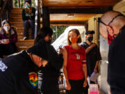 Holden Village resident Krista Mathistad, center, is about to receive a Moderna COVID-19 vaccine administered by paramedic Mistaya Johnston on a porch of their community building on Tuesday, March 30, 2021. Behind Mathistad are others who have been vaccinated or waiting for their vaccine.