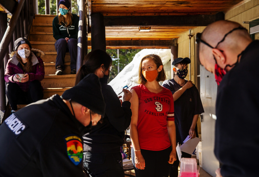 Holden Village resident Krista Mathistad, center, is about to receive a Moderna COVID-19 vaccine administered by paramedic Mistaya Johnston on a porch of their community building on Tuesday, March 30, 2021. Behind Mathistad are others who have been vaccinated or waiting for their vaccine.