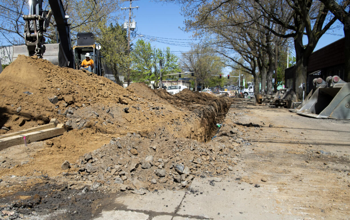 Workers tear up the road and excavate a trench along Broadway on Tuesday. A three-block section of the street has been closed off for a project to replace the more than century-old sewer and water main lines beneath the road. The full project will cover the Broadway corridor from East 13th Street to McLoughlin Boulevard.