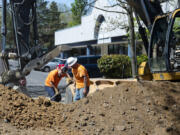 A pair of construction workers shovel large chunks of pavement into the excavator on Tuesday at the corner of Broadway and East Mill Plain Boulevard. The work marks the start of a project to replace the sewer and water main lines beneath Broadway, which will continue through the summer.