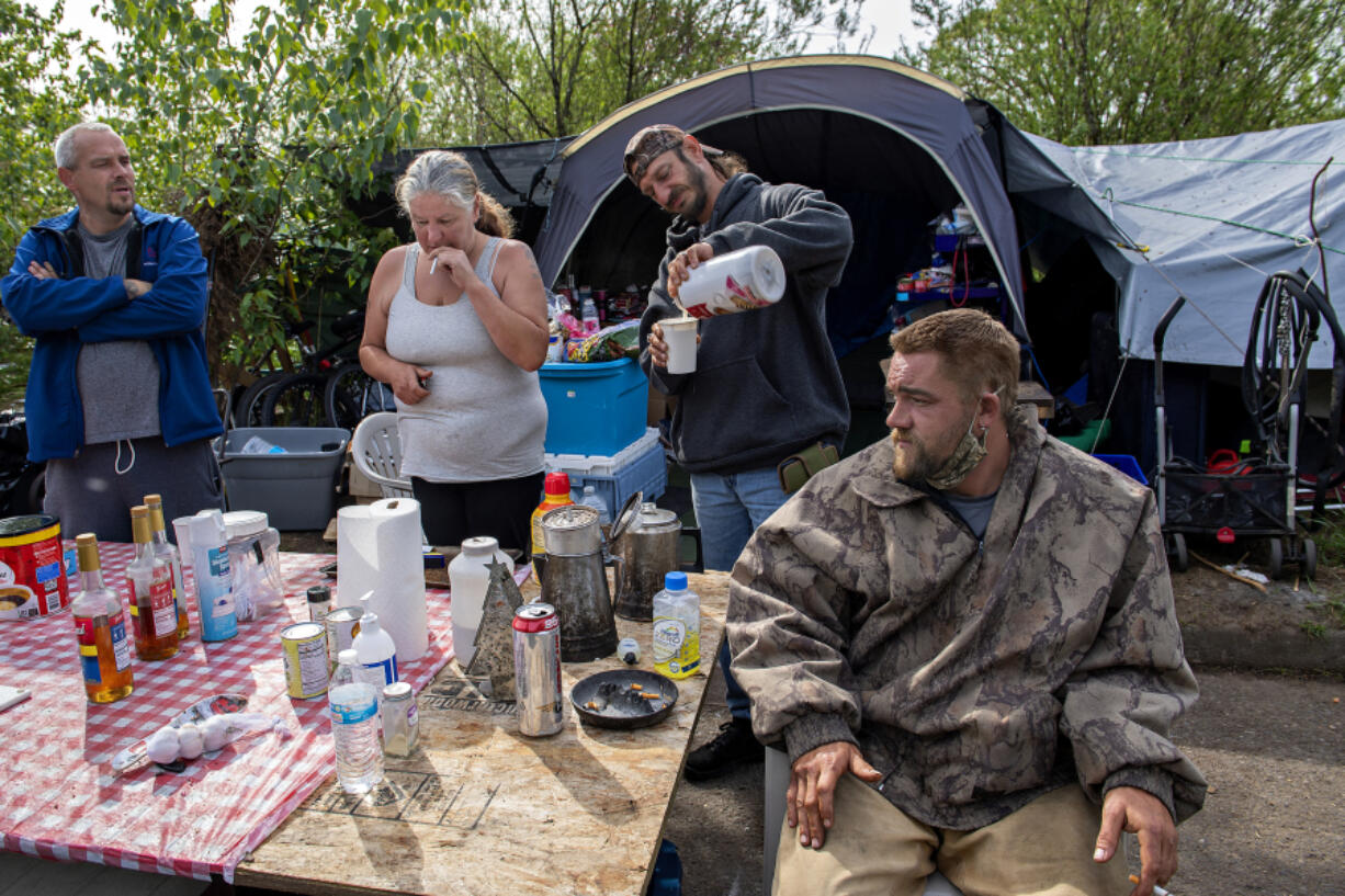 David Neff, from left, joins Rae Mackmer, John McKishen and Nathan Berney as they watch the cleanup at the homeless encampment in east Vancouver on Thursday morning. Vancouver is trying to remove garbage from homeless encampments while improving its relationship with its unhoused population.