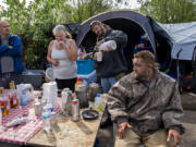 David Neff, from left, joins Rae Mackmer, John McKishen and Nathan Berney as they watch the cleanup at the homeless encampment in east Vancouver on Thursday morning. Vancouver is trying to remove garbage from homeless encampments while improving its relationship with its unhoused population.