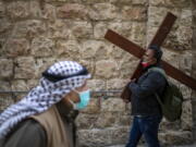 A Christian carries a cross as he walks along the Via Dolorosa towards the Church of the Holy Sepulchre, traditionally believed by many to be the site of the crucifixion of Jesus Christ, during the Good Friday procession in Jerusalem&#039;s old city, Friday, April 2, 2021.