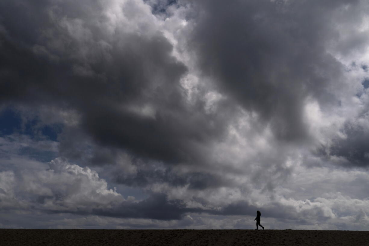 A woman strolls along the beach under rain clouds March 10 in Seal Beach, Calif. Rainstorms grew more erratic across most of the West over the past 50 years. (jae c.