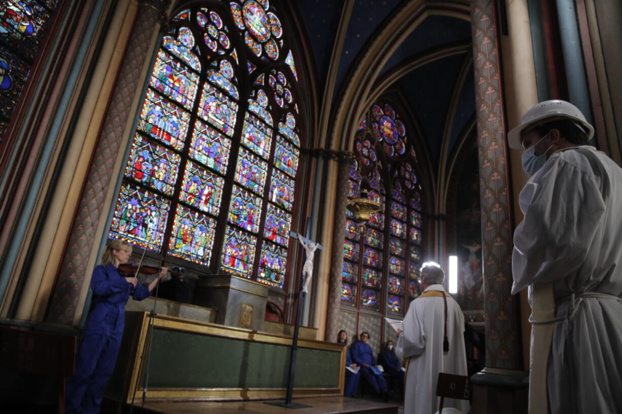 Notre Dame rector Patrick Chauvet, second right, stands as part of the Maundy Thursday ceremony, while cellist Marina Chiche, left, performs in Notre Dame Cathedral, Thursday, April 1, 2021, almost two years after a massive fire ravaged the Gothic cathedral.