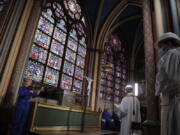 Notre Dame rector Patrick Chauvet, second right, stands as part of the Maundy Thursday ceremony, while cellist Marina Chiche, left, performs in Notre Dame Cathedral, Thursday, April 1, 2021, almost two years after a massive fire ravaged the Gothic cathedral.