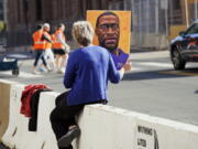 A woman holds a George Floyd picture while seated on a concrete barrier near the Hennepin County Government Center Monday, April 5, 2021, in Minneapolis where the second week of testimony in the trial of former Minneapolis police officer Derek Chauvin continues. Chauvin is charged with murder in the death of George Floyd during an arrest last May in Minneapolis.