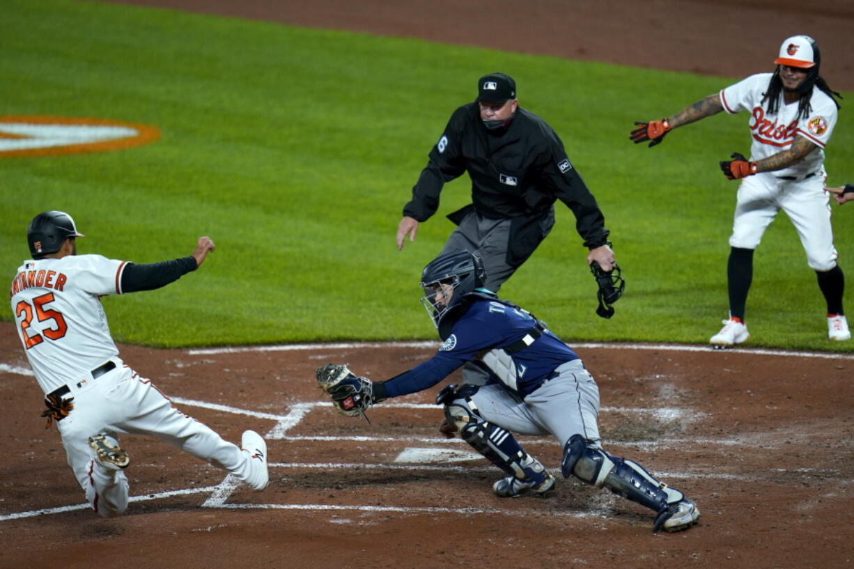 Baltimore Orioles&#039; Anthony Santander (25) slides into home as Seattle Mariners catcher Luis Torrens tries to apply the tag during the third inning of the second game of a baseball doubleheader, Tuesday, April 13, 2021, in Baltimore. The ball kicked away from from Torrens and Santander was ruled safe. On the play, Santander, Freddy Galvis and DJ Stewart scored on a bases loaded double by Maikel Franco.