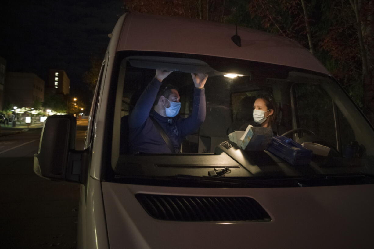 In this Oct. 2020 photo, Crisis Workers, Emergency Medical Technicians (EMTs), Henry Cakebread and Ashley Barnhill-Hubbard with CAHOOTS, a mental health crisis intervention program, discuss their last encounter during their night shift in Eugene, Ore. When police respond to a person gripped by a mental health or drug crisis, the encounter can have tragic results. Now a government health program will help communities set up an alternative: mobile teams of practitioners trained in de-escalating such potentially volatile situations.