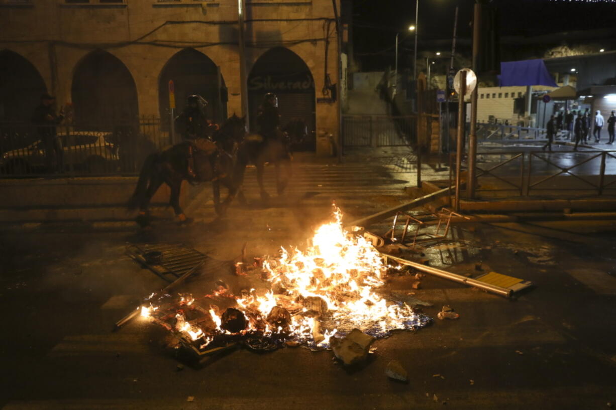 In this Thursday, April 22, 2021 file photo, mounted Israeli police officers ride past a fire during clashes with Palestinians, just outside Jerusalem's Old City. A year of relative calm between Israel and the Palestinians has come to an abrupt halt in recent days with the eruption of nightly clashes between Arab youths and Israeli police in east Jerusalem and a heavy barrage of rocket fire launched from the Hamas-ruled Gaza Strip.