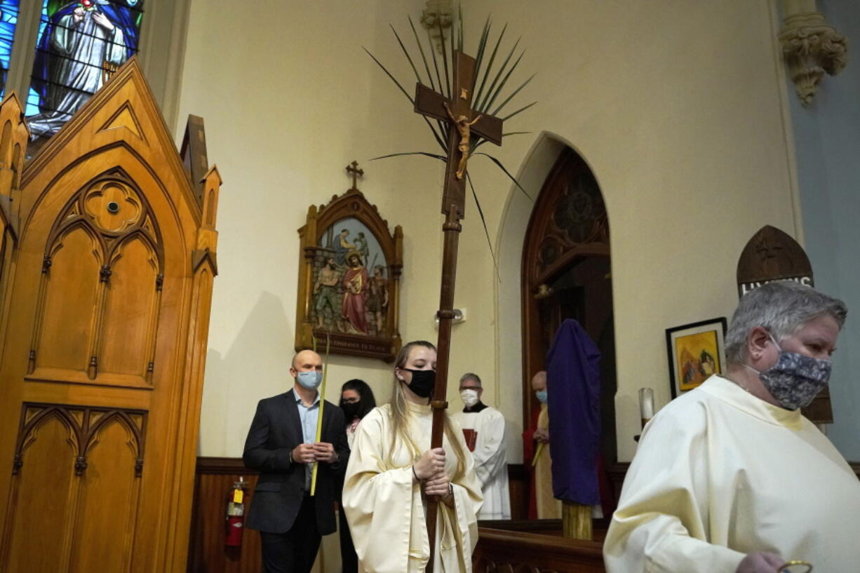 FILE - In this Sunday, March 28, 2021 file photo, altar server Samantha Holmes, of East Brookfield, Mass., center, carries a crucifix with palm leaves during a procession at the start of Palm Sunday Mass at Mary, Queen of the Rosary Parish in Spencer, Mass. For Christians across the United States, Easter services on Sunday will reflect an extra measure of joy as the nation experiences rising optimism after a year of pandemic.