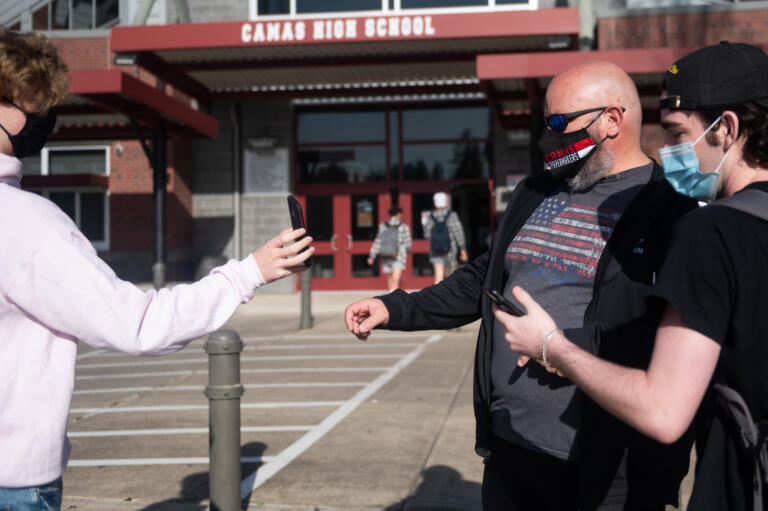 Camas High School staff member Dale Rule, center, checks health screeners on studentsÕ phones before they enter the building for class on Monday, April 19, 2021. Camas returned to four-day-a-week in-person instruction on Monday.