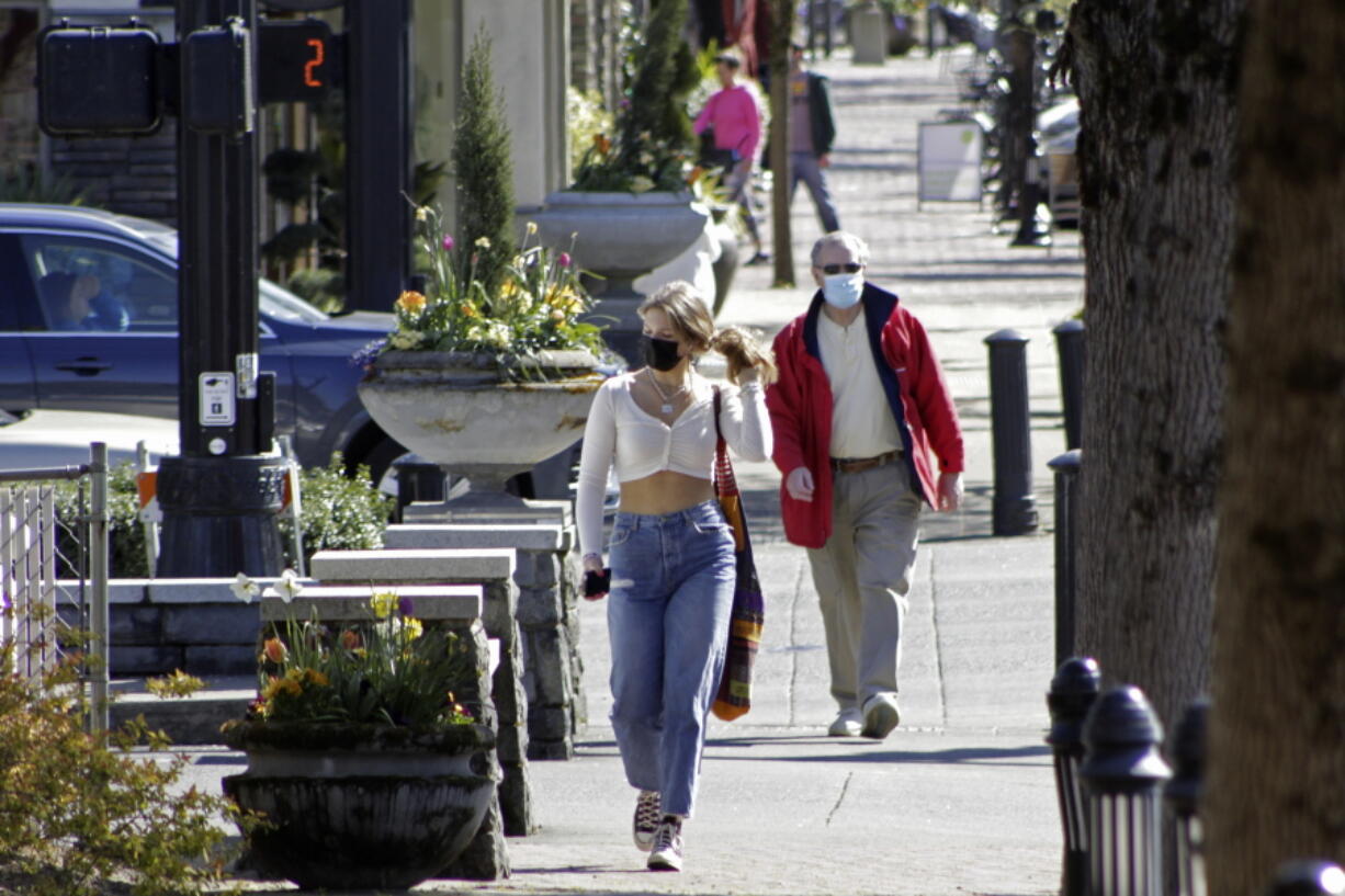 FILE - In this April 11, 2021, file photo, residents wearing masks walk in downtown Lake Oswego, Ore. Oregon Gov. Kate Brown said Tuesday, April 27, 2021 rising COVID-19 hospitalizations threaten to overwhelm doctors and she is moving 15 counties into extreme risk category, which imposes restrictions including banning indoor restaurant dining.