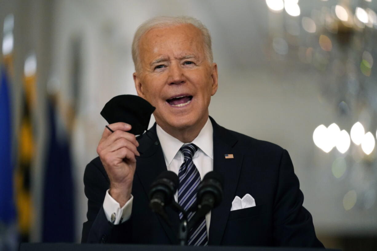 FILE - In this March 11, 2021, file photo, President Joe Biden holds up his face mask as he speaks about the COVID-19 pandemic during a prime-time address from the East Room of the White House in Washington. The U.S. is meeting President Joe Biden's latest vaccine goal of administering 200 million COVID-19 shots in his first 100 days in office, as the White House steps up its efforts to inoculate the rest of the public.