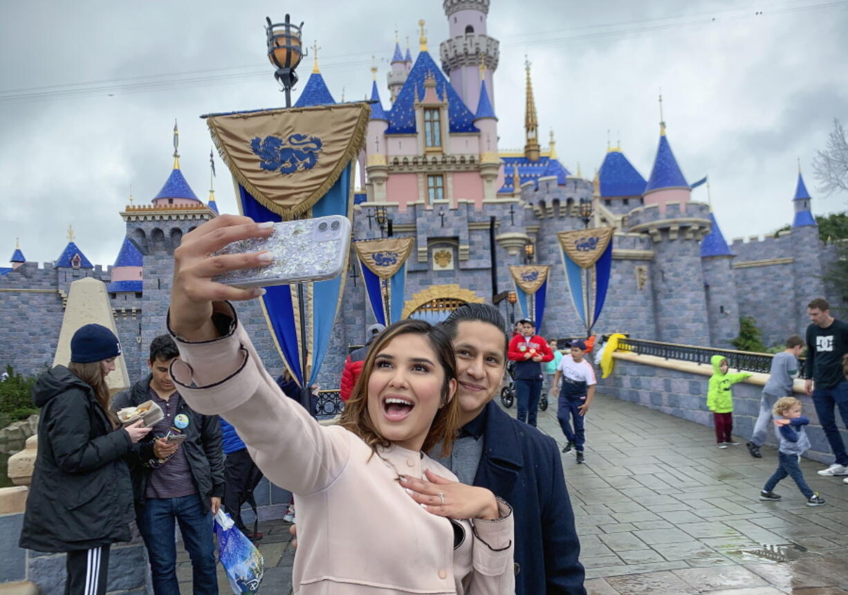 FILE - In this March 13, 2020, file photo, Katherine Quezada shows off her engagement ring as she takes a selfie with her new fiance, Fernando Carranza, in front of Sleeping Beauty Castle the during the last day before Disneyland closes because of the COVID-19 coronavirus outbreak, in Anaheim, Calif. Carranza proposed to Quezada in front of the castle earlier that day. Disneyland Park and Disney California Adventure park will reopen to visitors on Friday, April 30, 2021.