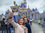 FILE - In this March 13, 2020, file photo, Katherine Quezada shows off her engagement ring as she takes a selfie with her new fiance, Fernando Carranza, in front of Sleeping Beauty Castle the during the last day before Disneyland closes because of the COVID-19 coronavirus outbreak, in Anaheim, Calif. Carranza proposed to Quezada in front of the castle earlier that day. Disneyland Park and Disney California Adventure park will reopen to visitors on Friday, April 30, 2021.