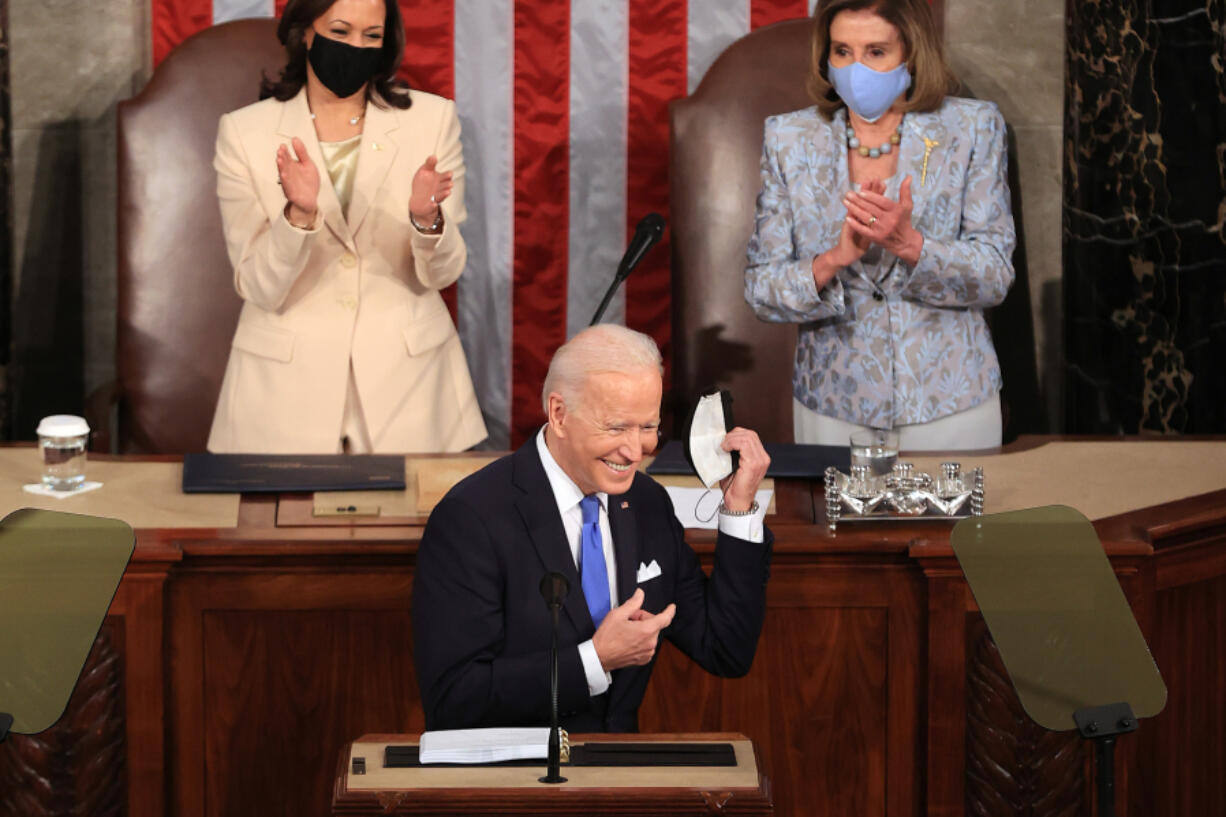 U.S. President Joe Biden removes his face mask before addressing a joint session of Congress as Vice President Kamala Harris, left, and Speaker of the House U.S. Rep. Nancy Pelosi (D-CA) look on in the House chamber of the U.S. Capitol April 28, 2021 in Washington, DC.