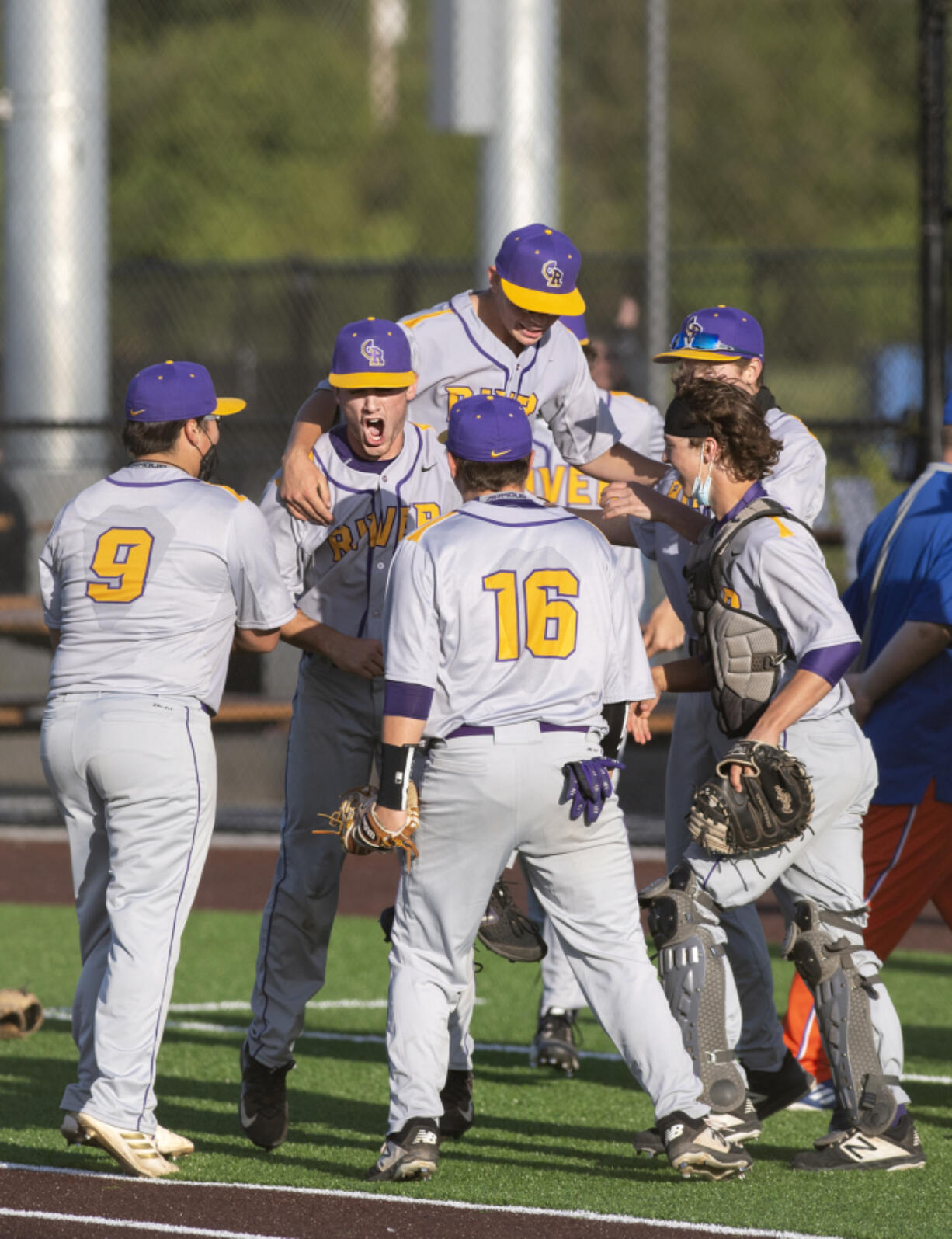 Columbia River players gather around pitcher Nick Alder, center, to celebrate a victory over Ridgefield on Tuesday, May 4, 2021, at the Ridgefield Outdoor Recreation Complex. Columbia River won 4-2 to advance in the 2A Southwest District Tournament.