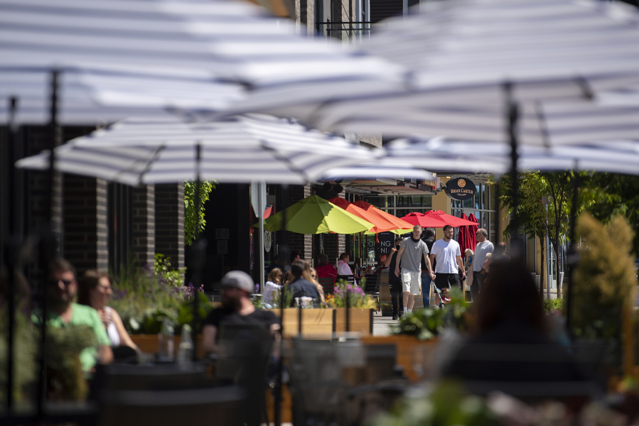 Colorful umbrellas provide shade for residents and visitors at The Waterfront Vancouver as they enjoy the sunshine with tasty food and a glass of wine Tuesday afternoon. Clark County has fewer restrictions on activities than the rest of the Portland metro area, and local restaurants have seen an influx of customers from Oregon as a result.