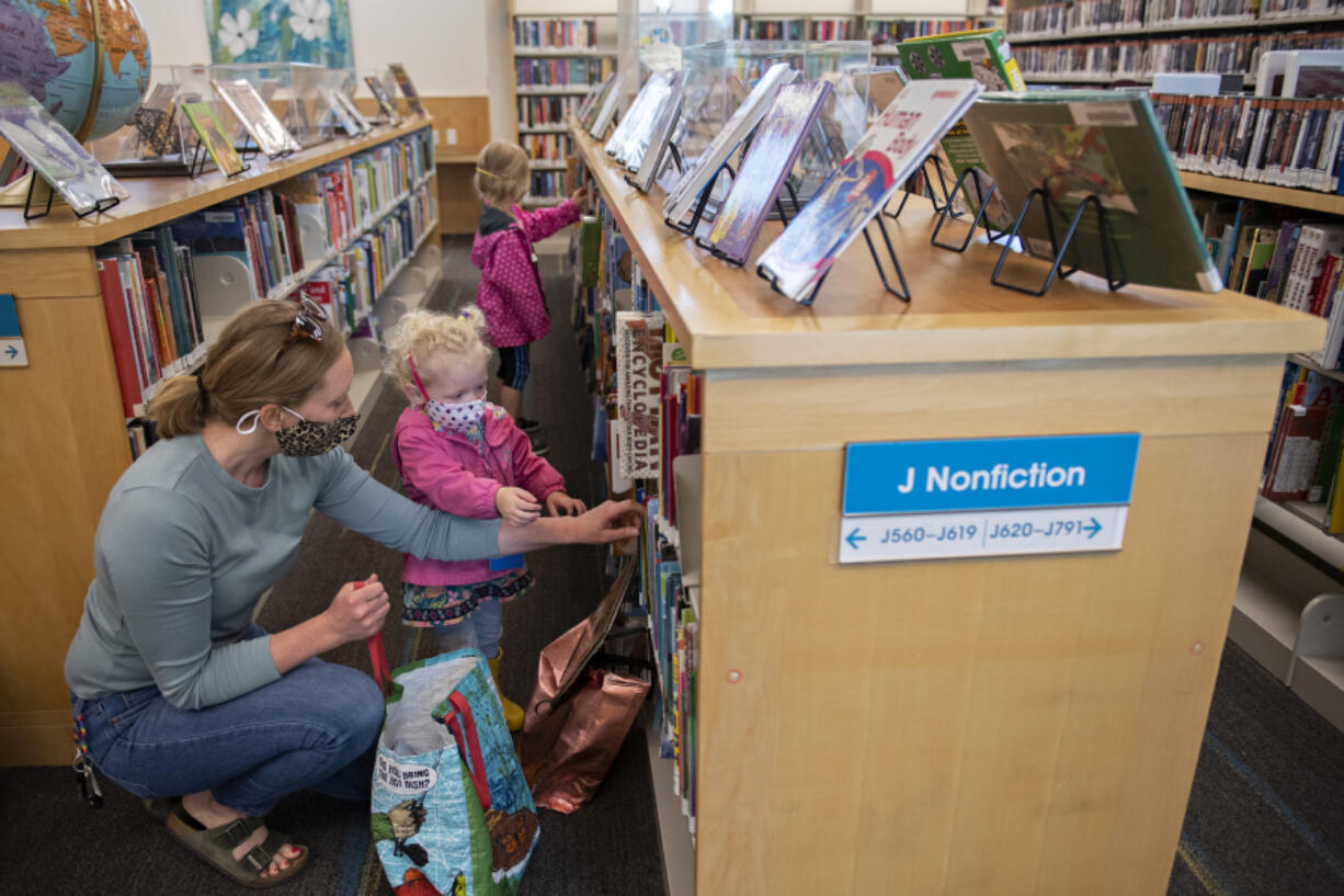 Tami Widmer joins her daughters Dakota, 2, and Willow, 4, in picking out some fun children's books at Three Creeks Community Library on Monday morning. Monday was the first day the library was open for limited visits in person since March 2020.  At top, stuffed animals wear masks too as literary classics are displayed at the front of the library on Monday morning.