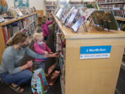 Tami Widmer joins her daughters Dakota, 2, and Willow, 4, in picking out some fun children's books at Three Creeks Community Library on Monday morning. Monday was the first day the library was open for limited visits in person since March 2020.  At top, stuffed animals wear masks too as literary classics are displayed at the front of the library on Monday morning.