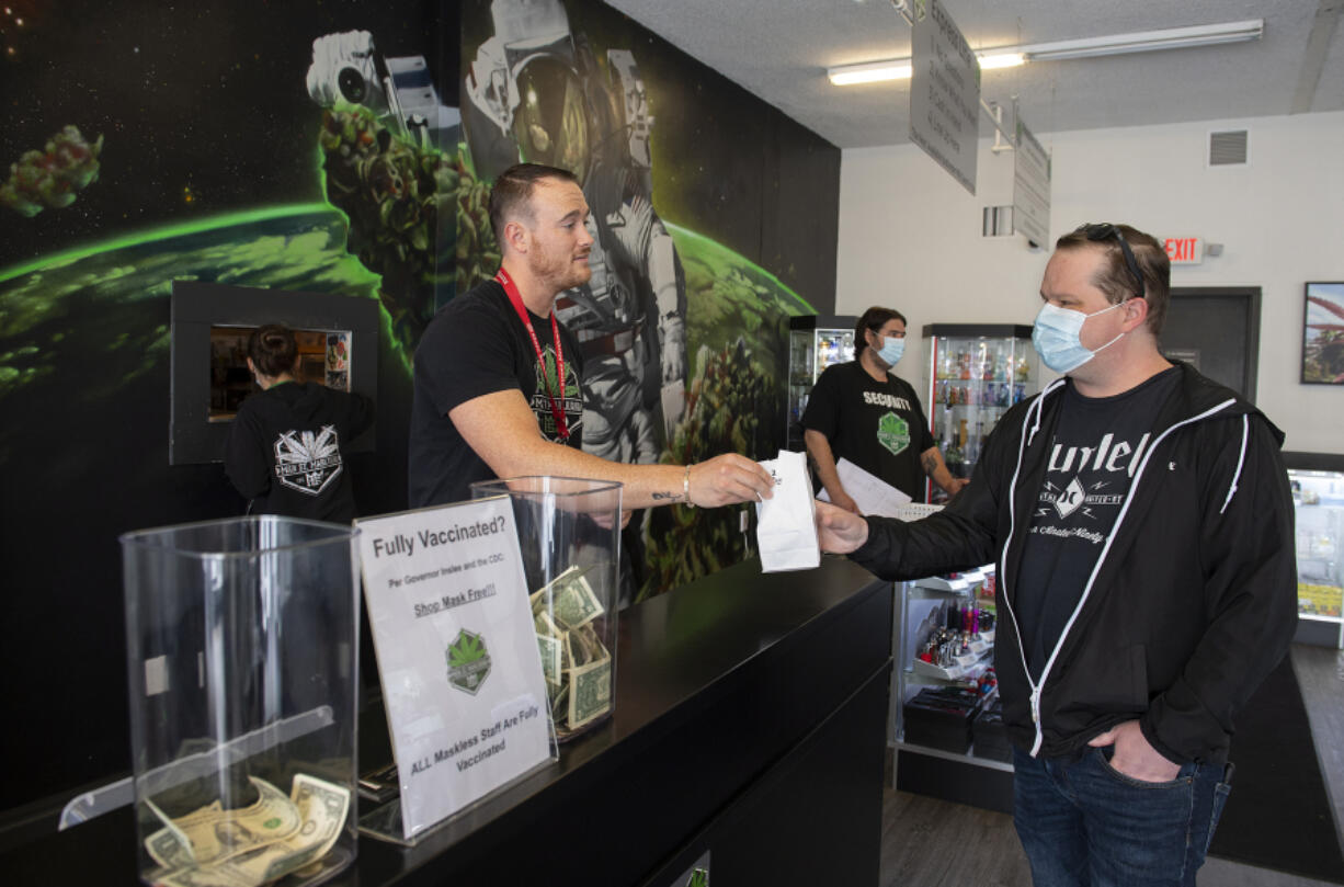 Main Street Marijuana cashier Josh Cecil, left, who is fully vaccinated, helps Tom Nicholson of Vancouver as he checks out in Uptown Village Tuesday morning. A number of signs are posted in the store informing customers that the staff are vaccinated and that masks are no longer required for vaccinated customers.
