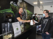 Main Street Marijuana cashier Josh Cecil, left, who is fully vaccinated, helps Tom Nicholson of Vancouver as he checks out in Uptown Village Tuesday morning. A number of signs are posted in the store informing customers that the staff are vaccinated and that masks are no longer required for vaccinated customers.