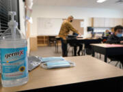 FILE - In this Feb. 2, 2021, file photo, hand sanitizer, wipes, and surgical masks rest on a desk in a fourth-grade classroom at Elk Ridge Elementary School in Buckley. Washington State authorities said Thursday, May 13, 2021, all schools in the state must provide full-time, in-person education for students for the 2021-22 school year and that students and staff will still be required to wear masks as a COVID-19 mitigation effort. (AP Photo/Ted S.