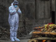 A relative in protective suit performs last rituals as the body of a person who died of COVID-19 is cremated in Gauhati, India, Monday, May 24, 2021. India crossed another grim milestone Monday of more than 300,000 people lost to the coronavirus as a devastating surge of infections appeared to be easing in big cities but was swamping the poorer countryside.